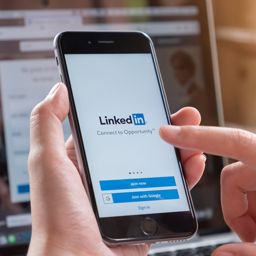 ein User hält ein Smartphone und drückt auf den Screen zur Anmeldung bei LinkedIn