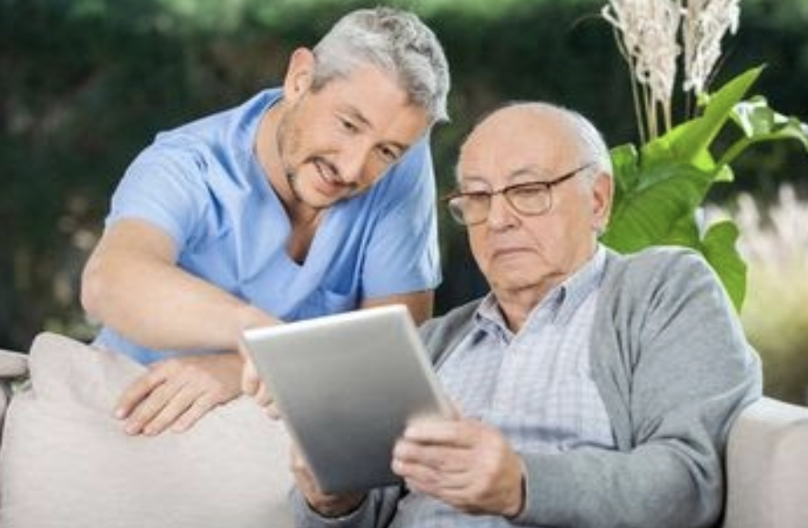 Ein Mann zeigt einem älteren Mann etwas auf einem Tablet – beide schauen interessiert auf den Bildschirm