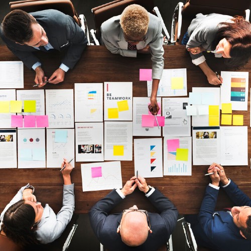 Sechs Personen beraten sich an einem Tisch auf dem Papiere ausgebreitet sind