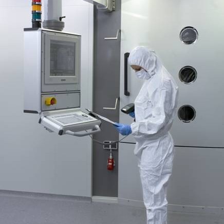 Eine Person in einem weißen Anzug und Schutzausrüstung bedient eine Maschine.