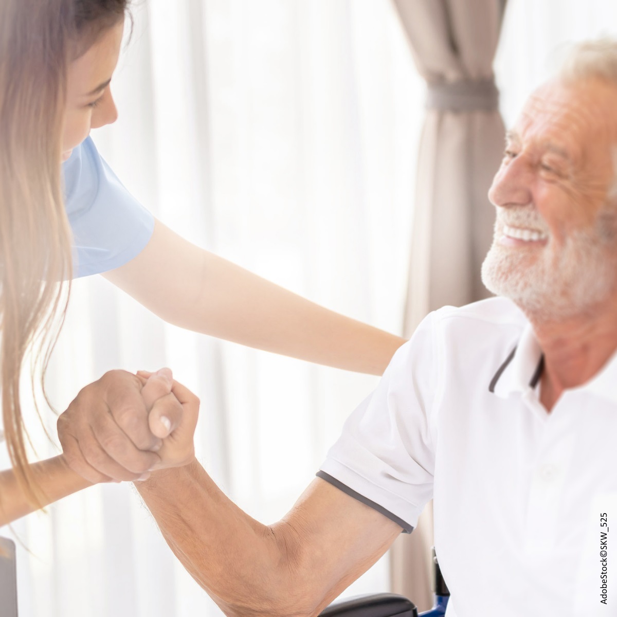 Ein Senior gibt einer jungen Pflegerin einen kräftigen Händedruck. Beide lachen dabei und sehen sehr freundlich und glücklich aus.