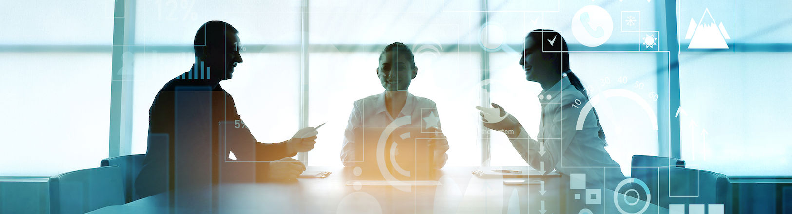 Das Bild zeigt drei Personen, die an einem Tisch in einem Besprechungsraum sitzen. Im Hintergrund sind große Fenster zu sehen, durch die natürliches Licht einfällt. Die Personen sind in eine Diskussion vertieft