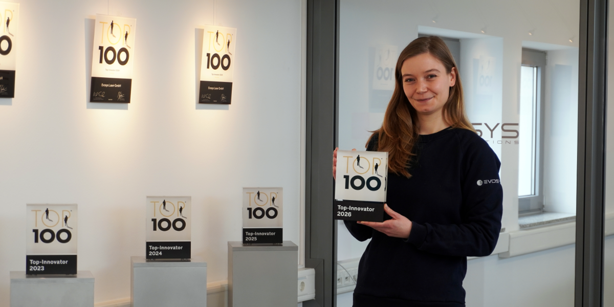 Frau in schwarzem Pullover hält eine Trophäe mit der Aufschrift 'Top-Innovator 2026' vor einer Wand mit weiteren Trophäen der Jahre 2019 bis 2025.