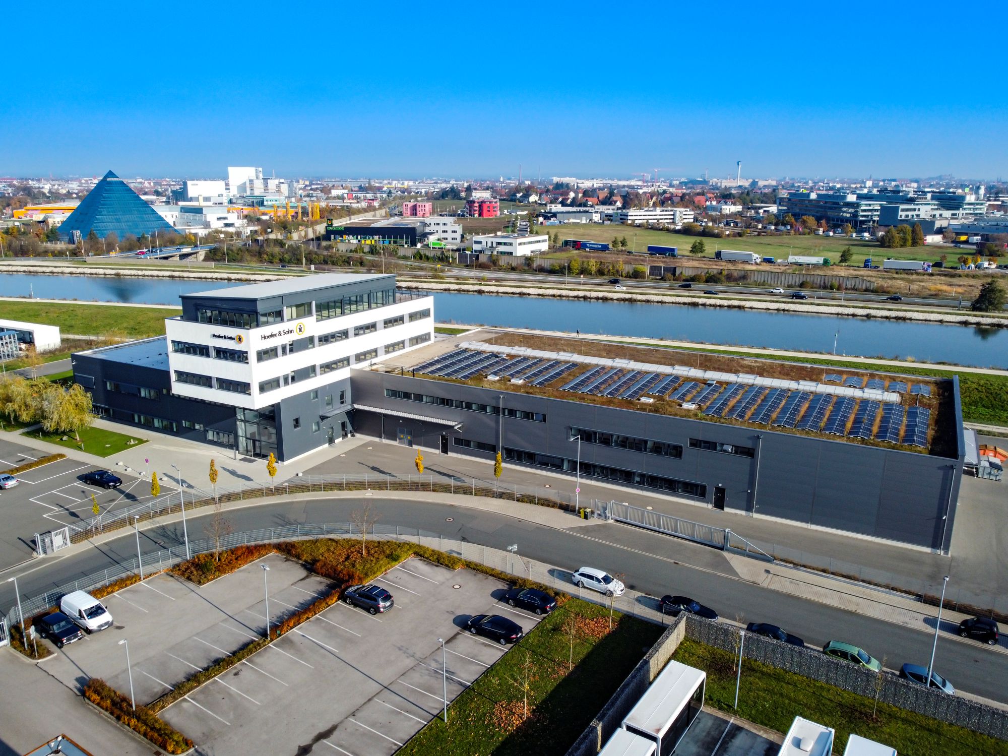 Luftaufnahme eines modernen Büro- und Industriegebäudes mit Solarpaneelen auf dem Dach an einem Kanal in einem Gewerbegebiet