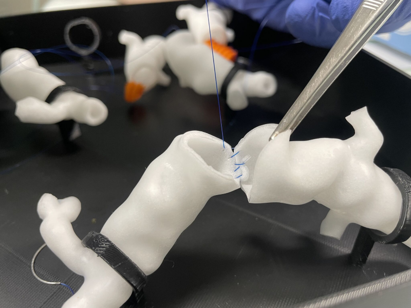 Das Bild zeigt eine weiße, skulpturartige Form vor einem schwarzen Hintergrund. Die Form ist unregelmäßig und geschwungen, mit mehreren Biegungen und Verzweigungen. Sie erinnert an eine abstrakte oder organische Struktur, möglicherweise inspiriert von natürlichen Formen wie Ästen oder Wurzeln.
