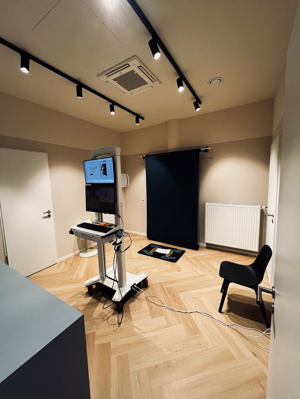 Raum mit medizinischem Gerät, schwarzem Hintergrund und Holzfußboden, Kabel am Boden sichtbar.