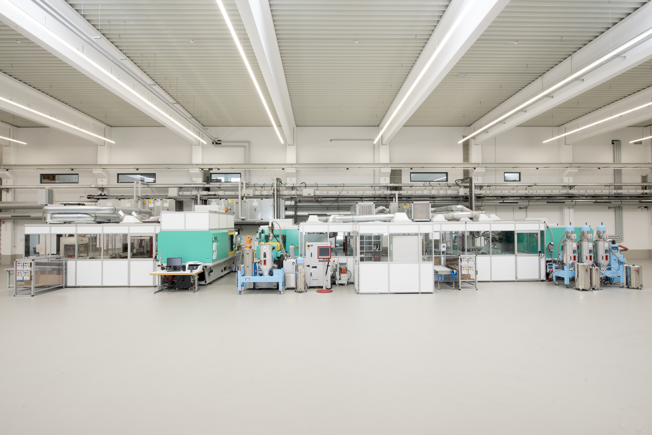 Große, helle Industriehalle mit mehreren blauen und weißen Maschinen in einer Reihe unter einer Decke mit sichtbaren Trägern und Leuchten