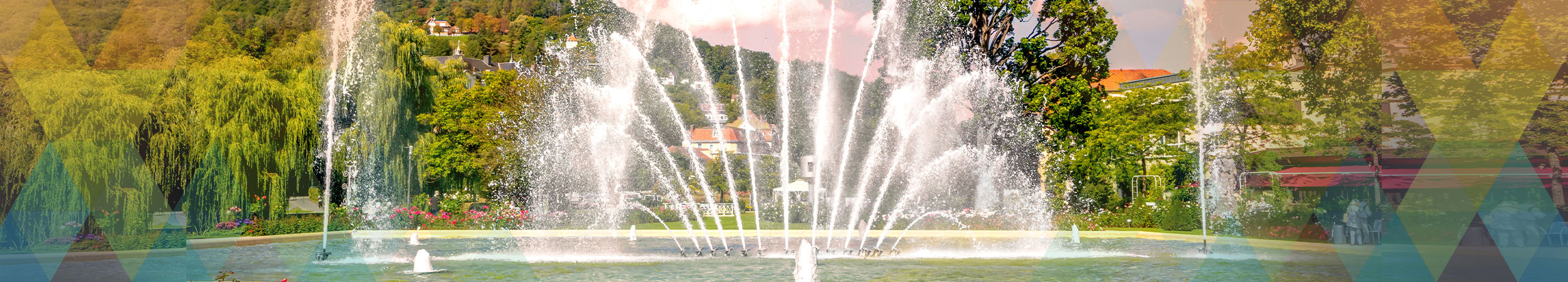 Parkanlage mit einem großen Brunnen aus dem Wasserfontänen nach oben schießen.