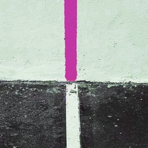 Eine minimalistische, grafische Darstellung von Linien auf einem strukturierten Untergrund. Eine weiße Linie verläuft vom dunklen Boden bis zur hellen Wand, wo sie auf eine senkrechte, magentafarbene Linie trifft.