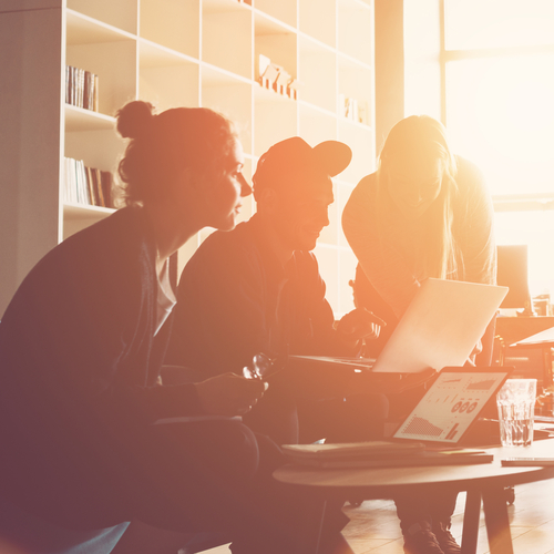 Eine Gruppe von Personen sitzt um einen Tisch mit Laptops und diskutiert angeregt.