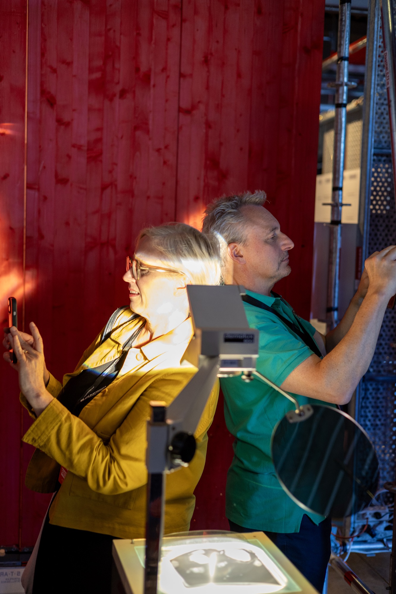 Eine Frau und Andreas Böhm, Innovationsnetzwerk Digitalisierung, Leitung ThinkNet Quantentechnologie, Bayern Innovativ GmbH, stehen Rücken an Rücken. Beide halten ein Handy in der Hand und machen ein Foto. Vor ihnen steht ein Tageslichtprojektor. Hinter ihnen ist eine rote Holzwand.