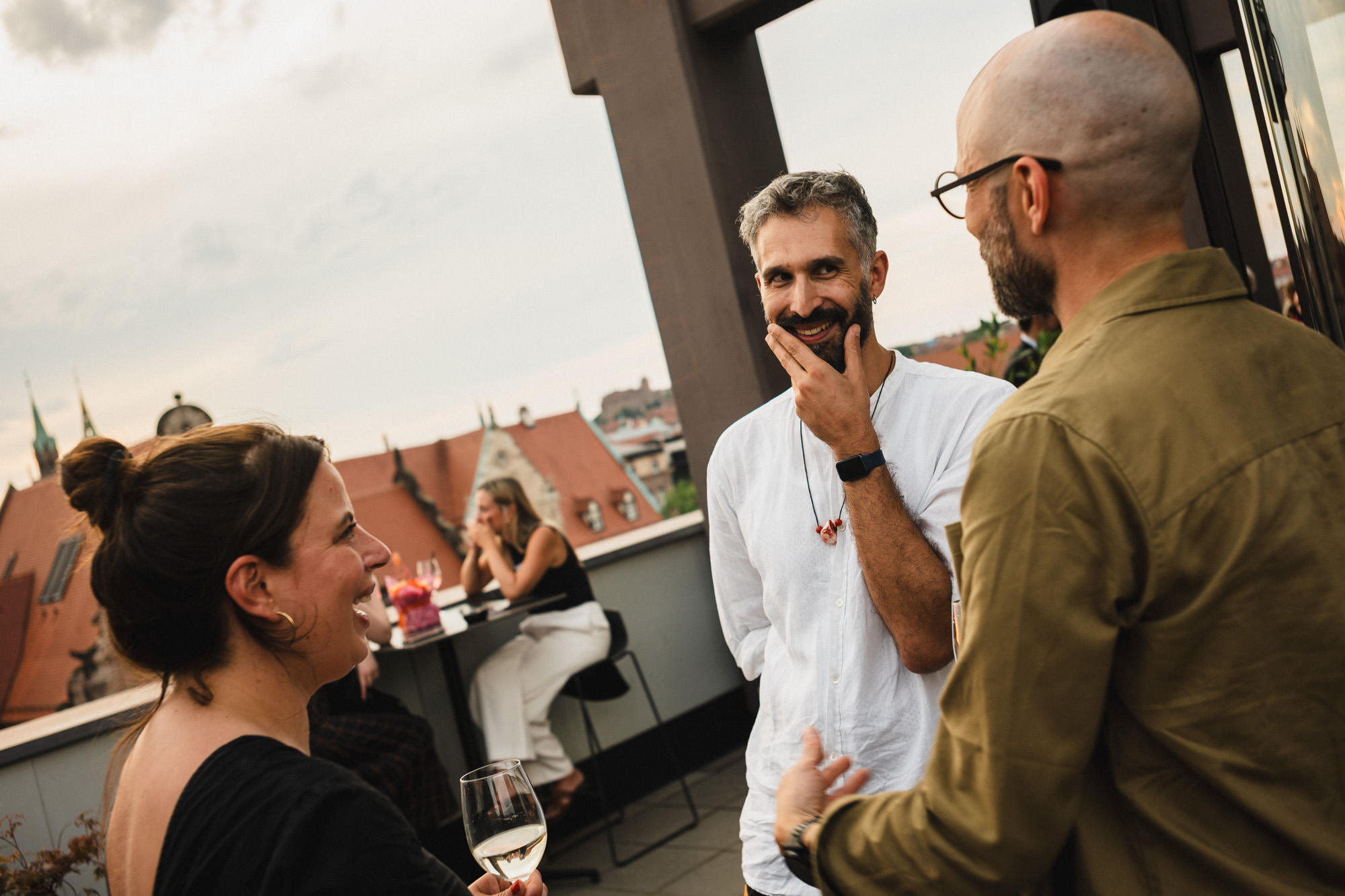 Andreas Auberger, Leitung Creative TechHUB der Bayern Innovativ GmbH, tauscht sich mit Christian Fayek von bayern design und einer weiteren Person auf der Daxhterrasse aus. Im Hintergrund sind die Nürnberger Altstadt und weitere Gäste zu sehen.