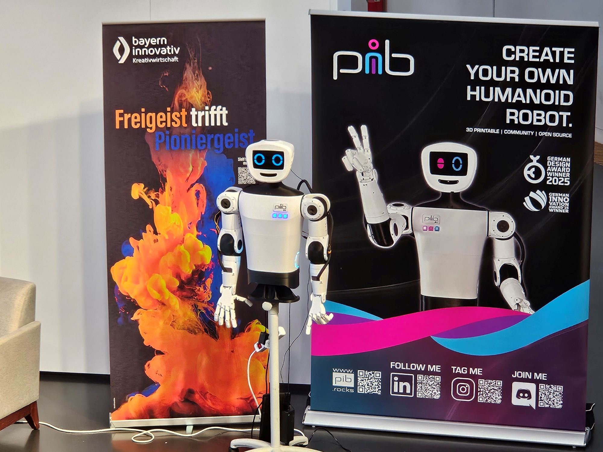 Vor zwei Roll-ups ist ein pib (printable intelligent bot und ist ein 3D-druckbarer humanoider Roboter), zu sehen.