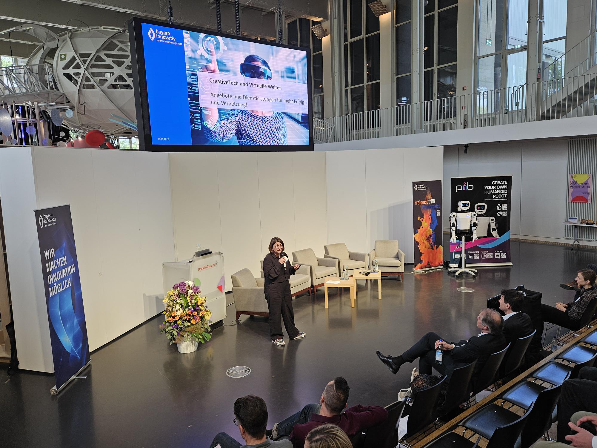 Ausblick CreativeTech 2026: Johanna Lison, Projektmanagerin des CreativeTechHUB, Bayern Innovativ GmbH, spricht vor Publikum in ein Mikrofon.