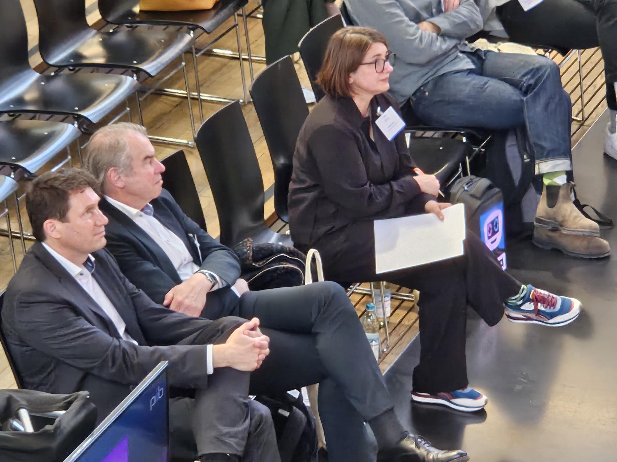 Markus Eder, Ministerialdirigent, Bayerischen Staatsministerium für Wirtschaft, Landesent-wicklung und Energie, Robert Bartl, Mitglied der Geschäftsleitung, Bayern Innovativ GmbH und Johanna Lison, Projektmanagerin CreativeTechHUB, Bayern Innovativ GmbH, sitzen nebeneinander im Publikum und hören zu.
