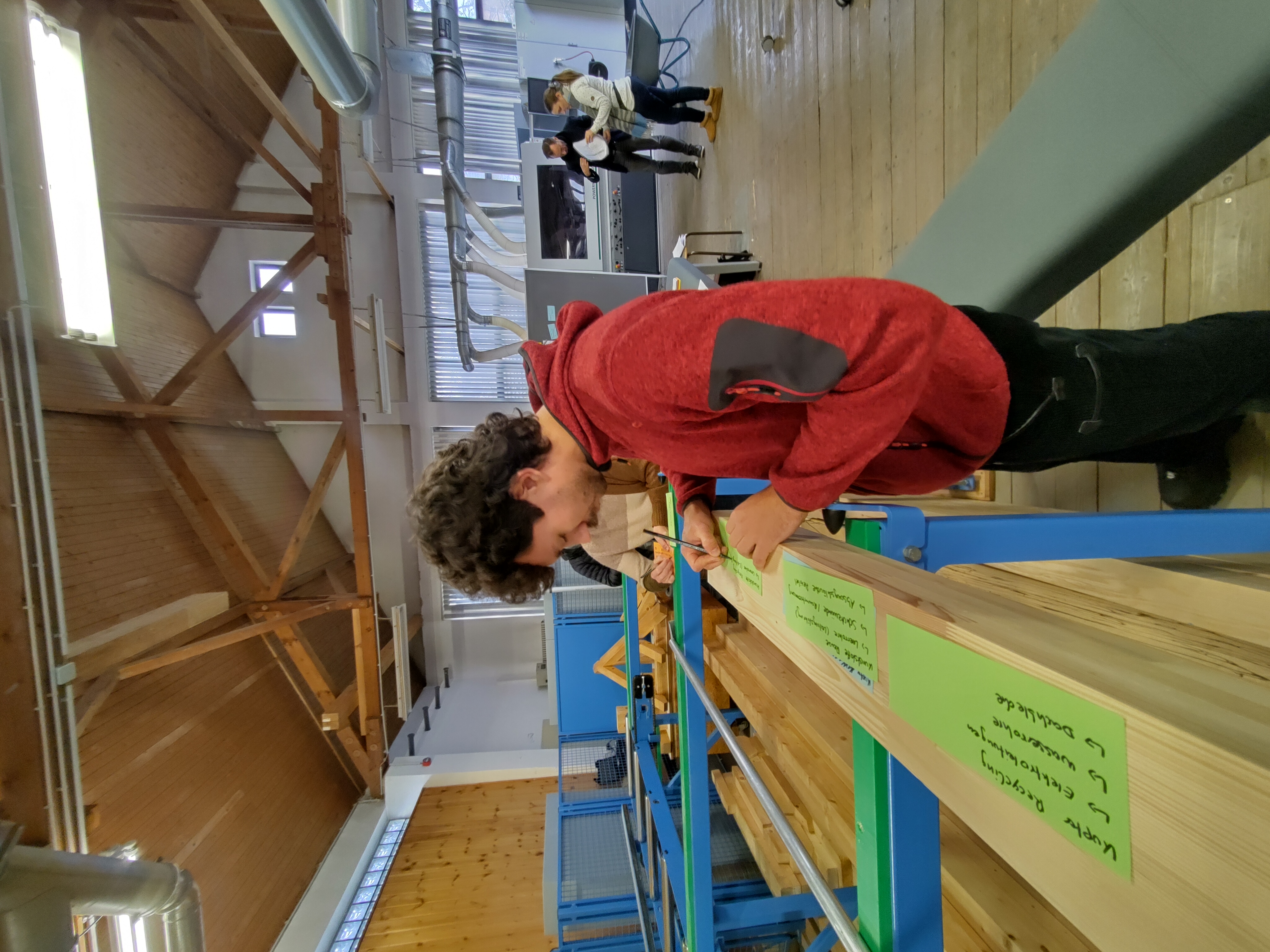 Ein Student erarbeitet etwas auf grünen Moderationskarten in einem Labor-Sägewerk. 