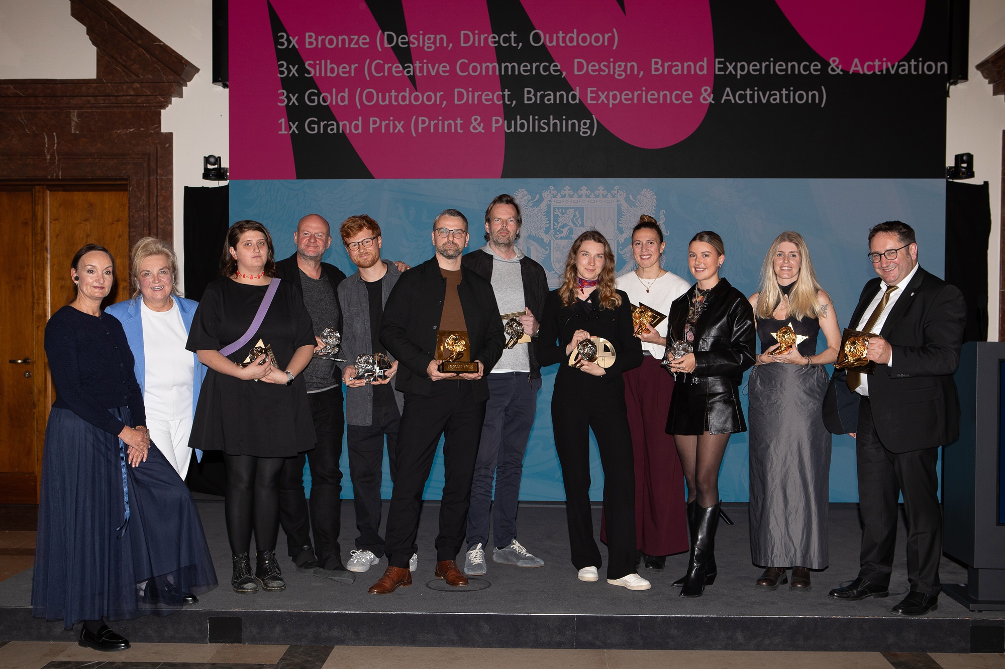 Tobias Gotthardt, Staatssekretär im Bayerischen Staatsministerium für Wirtschaft, Landesentwicklung und Energie, und Petra Lorenz, Geschäftsführerin des CommClubs Bayern e.V., stehen gemeinsam mit den bayerischen Gewinnern und Gewinnerinnen des diesjährigen Cannes Lions auf einer Bühne.