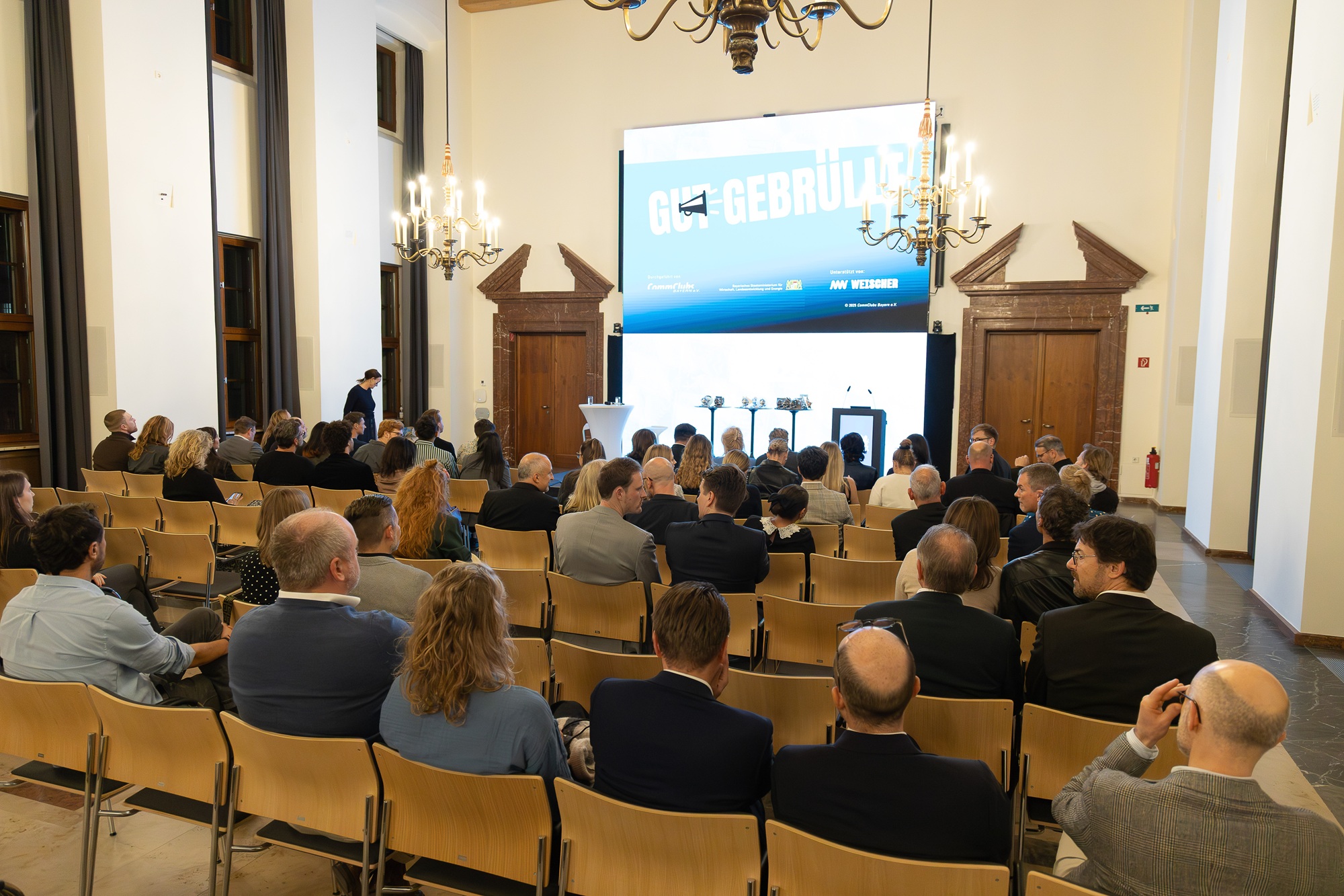 Der Veranstaltungssaal der Preisverleihung „Gut Gebrüllt“ 2025 ist zu sehen. Zahlreiche Gäste sitzen in Reihen und schauen nach vorne auf die Bühne, auf der ein Rednerpult steht.