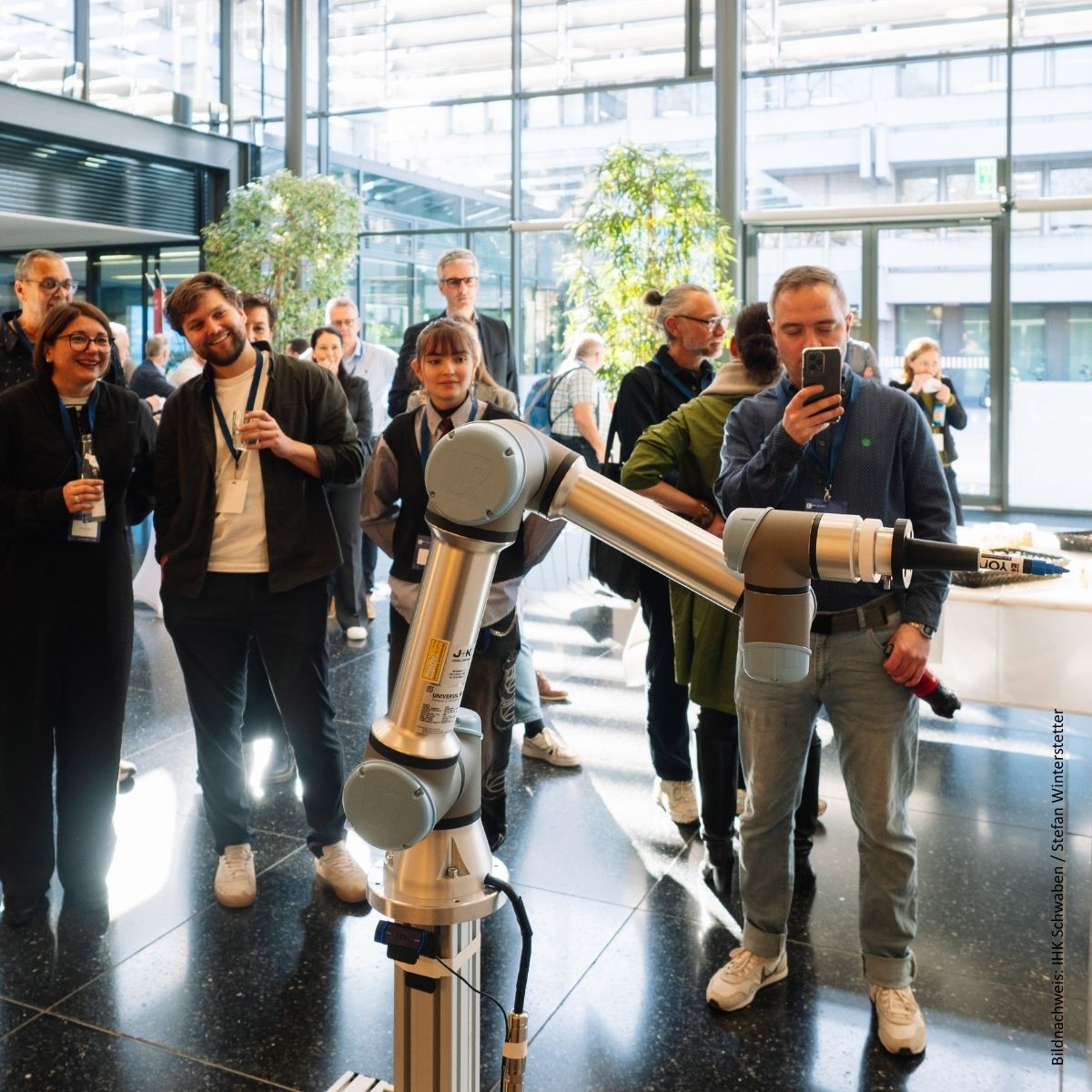Menschen stehen und fotografieren einen Roboterarm. 