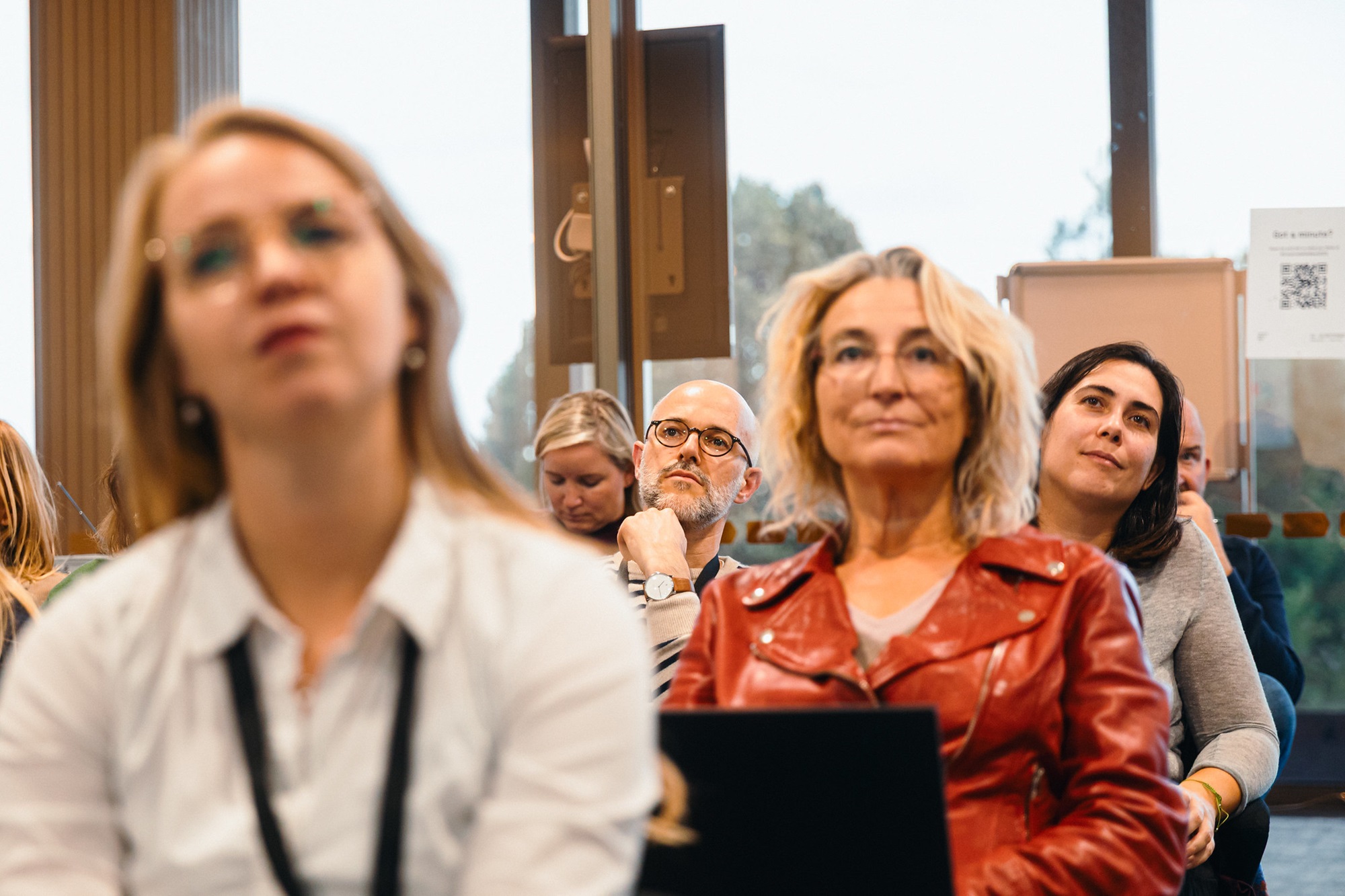 Mehrere Personen sitzen in einem Raum und hören einer Veranstaltung zu. Unter den Zuhörenden ist auch Henning Berthold, Projektleiter Analyse und Dialog, Innovationsnetzwerk Kreativwirtschaft der Bayern Innovativ GmbH, der nach vorne blickt.