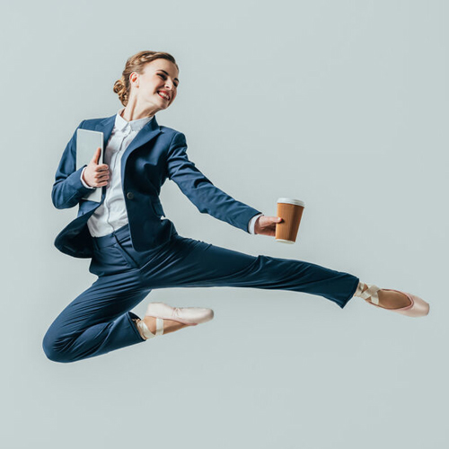 Eine Frau im Anzug springt in die Luft und strahlt Freude und Energie aus.