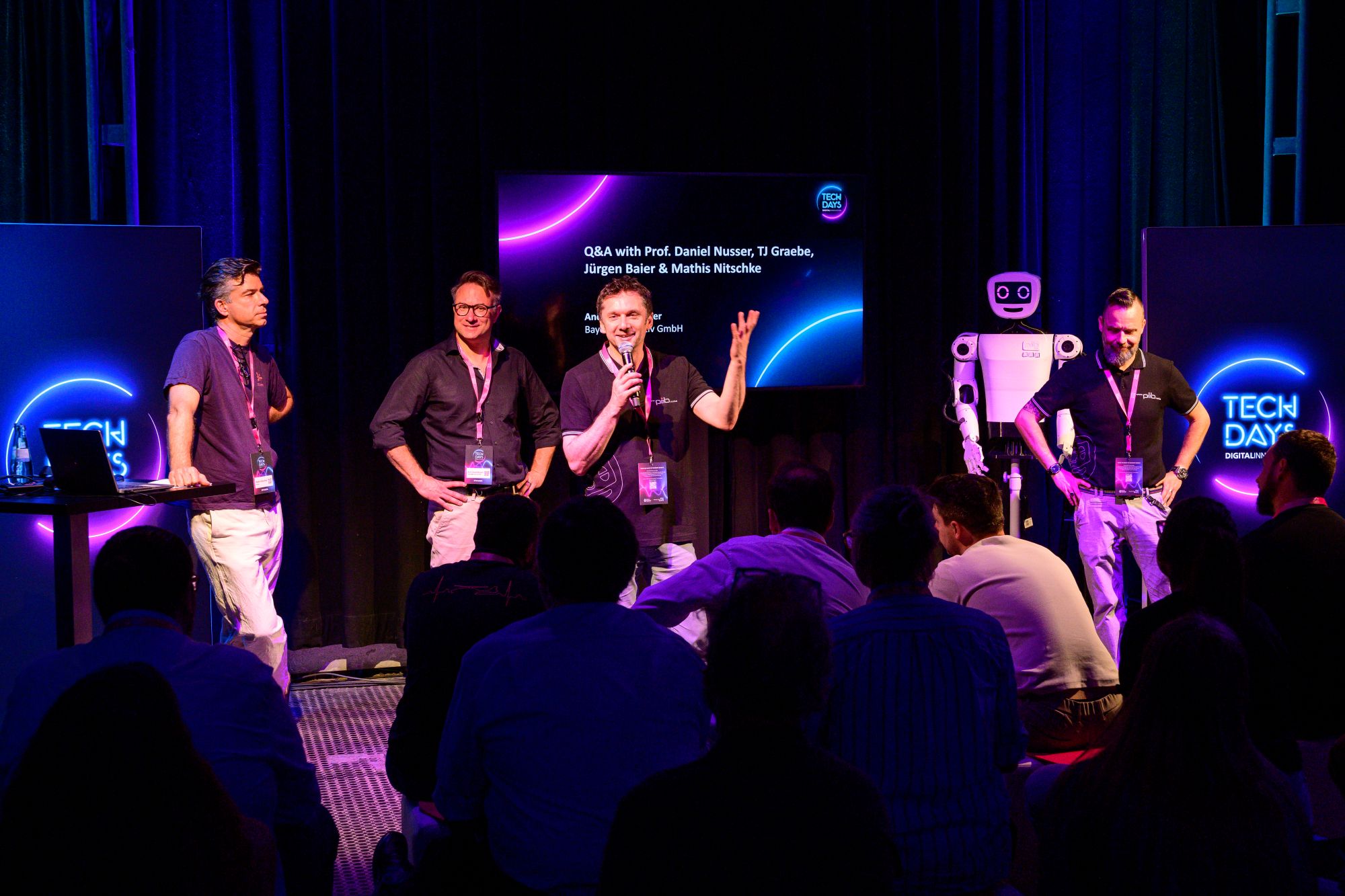 Mathis Nitschke, Director bei Sofilab, Prof. Daniel Nusser, Studiengangsleitung Pro-zess- und Produktdesign an der DIPLOMA Hochschule, Dr. Jürgen Baier, CEO der isen-to GmbH und TJ Graebe, Projektmanager Humanoide Robotik bei der isento GmbH führen auf einer Bühne vor Publikum eine Q&A-Runde durch.