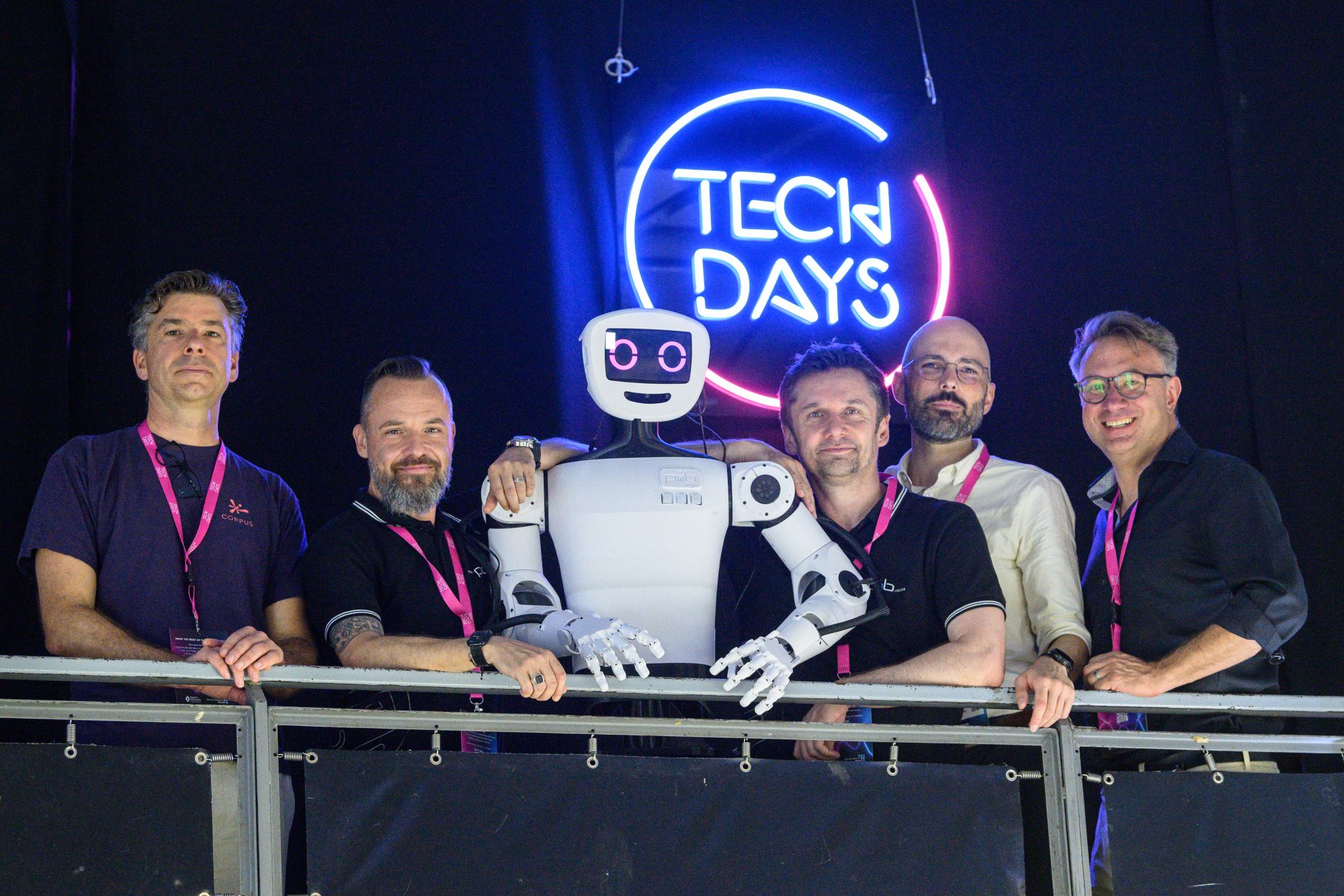 Mathis Nitschke, Director, Sofilab, TJ Graebe, Projektmanager Humanoide Robotik, isento GmbH, Dr. Jürgen Baier, CEO, isento GmbH, Andreas Auberger, Leitung CreativeTechHUB, Bay-ern Innovativ GmbH und Prof. Daniel Nusser, Studiengangsleitung Prozess- und Produktdesign, DIPLOMA Hochschule stehen gemeinsam mit einem humanoiden Roboter vor einem beleuch-teten „TECH DAYS“-Logo und blicken in die Kamera.