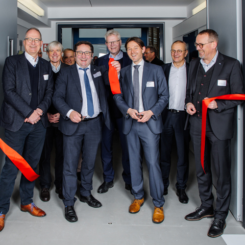 Mehrere Männer stehen hinter einem durchgeschnittenen Band und eröffnen ein neues Gebäude