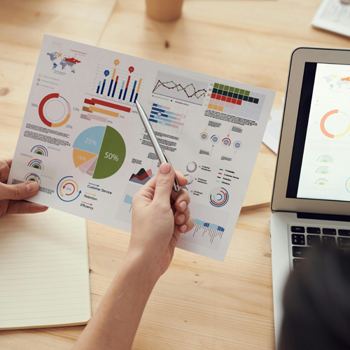 Eine Person hält einen Stift und betrachtet ein Blatt mit Grafiken und Diagrammen.
