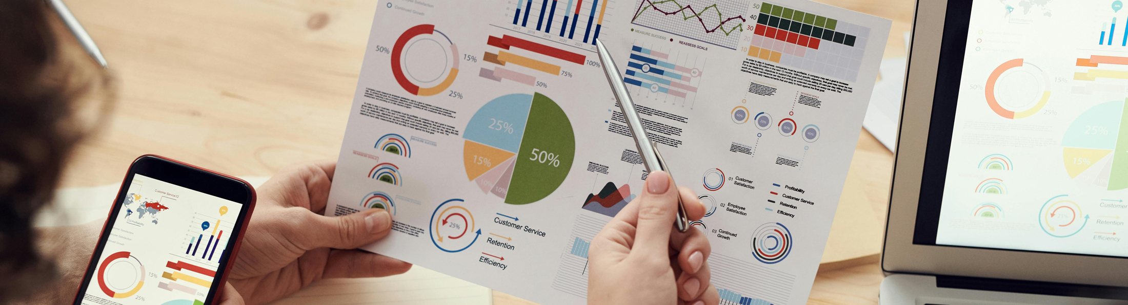 Eine Person hält einen Stift und betrachtet ein Blatt mit Grafiken und Diagrammen.