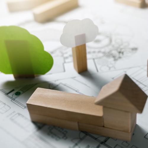 Holzblöcke und Papierausschnitte eines Hauses sowie von Bäumen auf einem Tisch angeordnet.