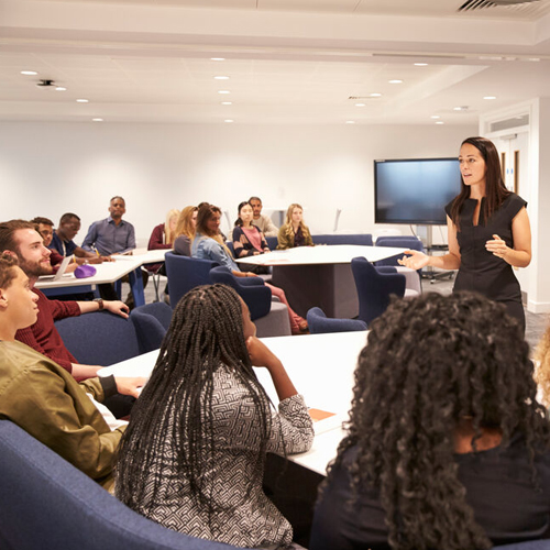 Eine Dozentin hält vor jungen Menschen einen Vortrag.