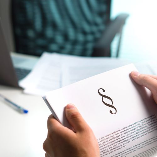 Person hält ein Dokument mit einem Paragrafenzeichen in den Händen. Im Hintergrund sind ein Schreibtisch mit Laptop, Unterlagen und einem Stift zu sehen.