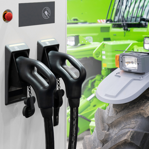 Im Vordergrund eine E-Ladestation, im Hintergrund stehen einige Traktoren