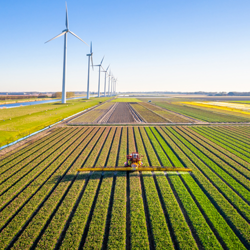 Ein Traktor bearbeitet ein Feld, während mehrere Windturbinen in der Ferne stehen.