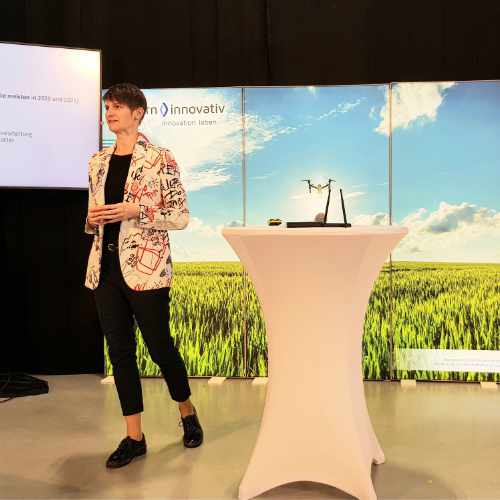 Zu sehen ist eine Referentin auf der Bühne, die Ihren Vortrag präsentiert