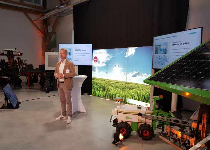 zu sehen ist die Bühne mit Stehtisch, einer Motivwand und einem Referenten vor einer Videoleinwand