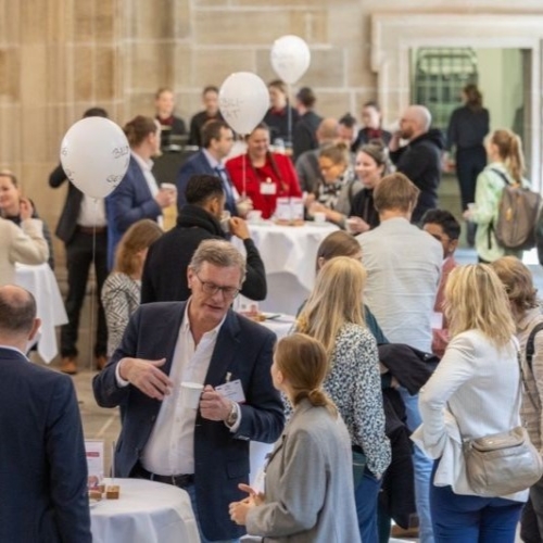 Menschen im Gespräch bei einer Netzwerkveranstaltung in einer historischen Halle mit Stehtischen und Luftballons.