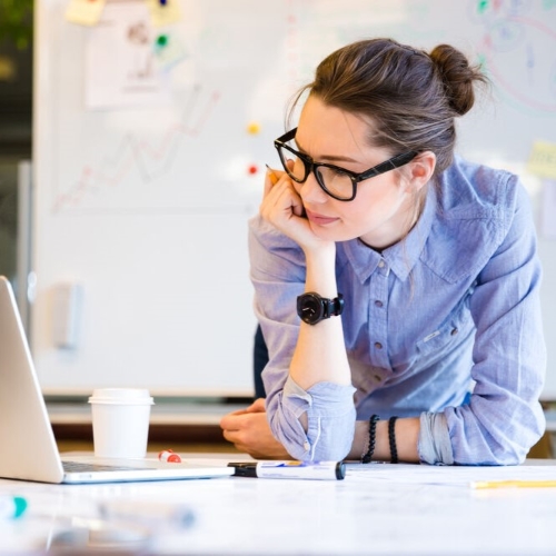 Eine professionell gekleidete Frau lehnt sich an einen Tisch und blickt konzentriert auf den Bildschirm ihres Laptops