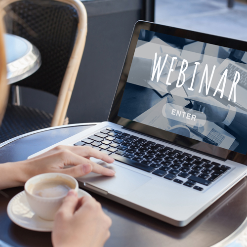Eine Frau sitzt vor dem Laptop und nimmt an einem Webinar teil.