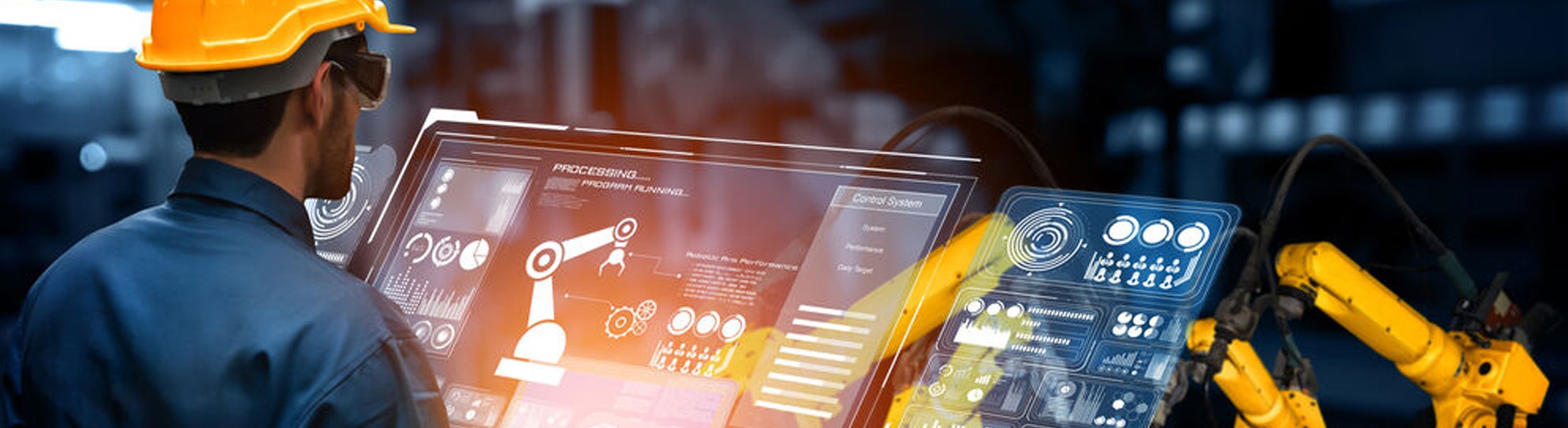 Ein Arbeiter mit Schutzhelm und Schutzbrille steht vor einem großen Display in einer Produktionshalle