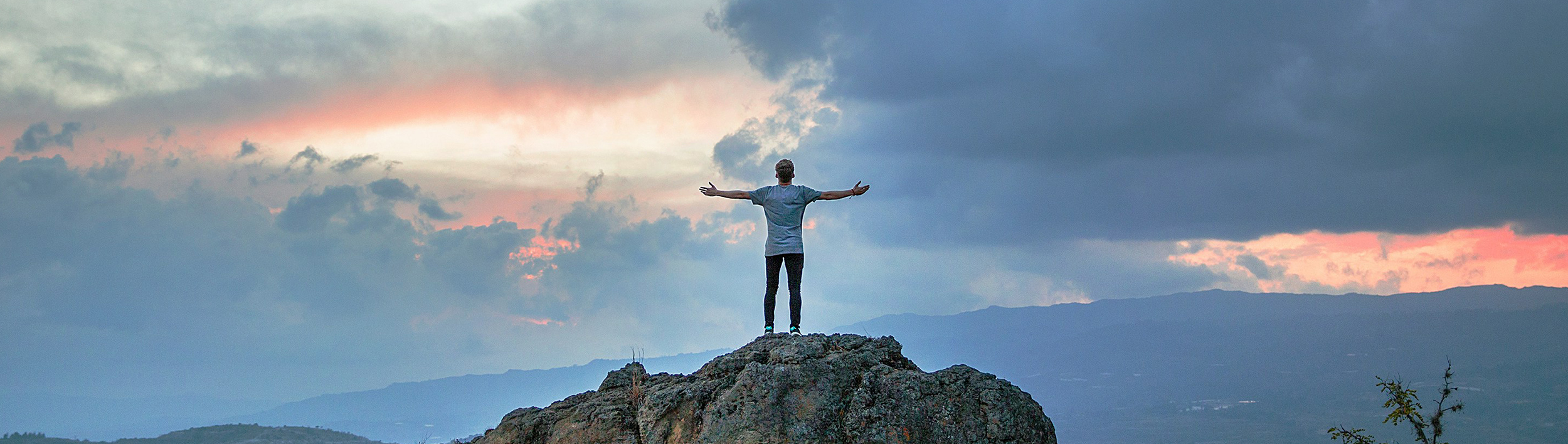 Ein Wanderer steht mit ausgestreckten Armen auf einem Berg