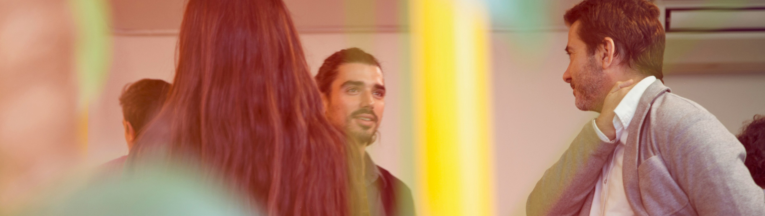 Mehrere Personen stehen im Gespräch in einem Innenraum, teilweise überlagert von farbigen Lichteffekten.