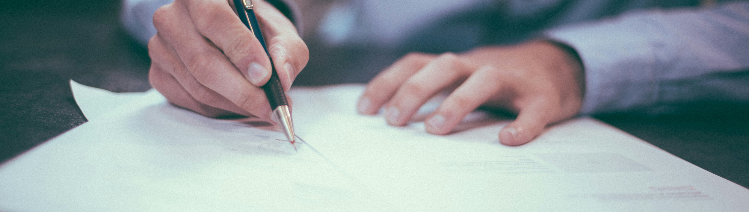 Die Hände von einem Mann im Hemd die gerade etwas unterschreiben