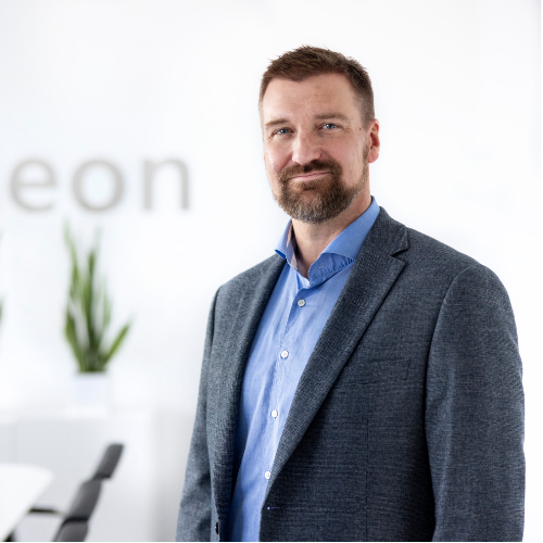 Person mit blauem Hemd und dunklem Blazer steht in einer büroähnlichen Umgebung.