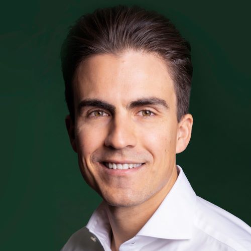 Auf dem Bild ist ein Mann mit dunklen, kurzen Haaren zu sehen. Er trägt ein weißes Hemd und lächelt freundlich.