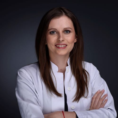 Auf dem Bild ist eine Frau mit dunklen Haaren und weißer Jacke zu sehen