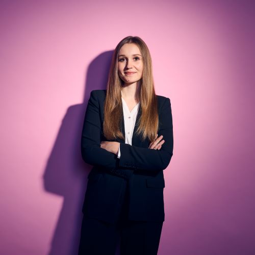 Auf dem Bild ist eine Frau mit langen Haaren zu sehen. Sie trägt einen schwarzen Hosenanzug.