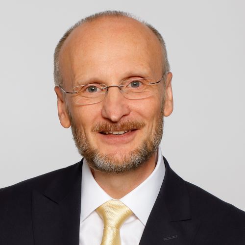 Auf dem Bild ist ein Mann mit dunklem Sakko und heller Krawatte zu sehen