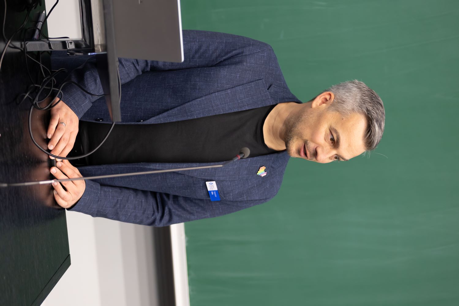  Ein Mann im Anzug steht vor einem schwarzen Brett und präsentiert Informationen.